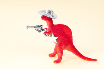 Close up of a small red toy dinosaur wearing a cowboy hat, holding a revolver in his arm and having...