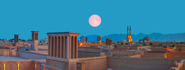 Historic City of Yazd with famous wind towers in the background full moon at twilight blue hour-...