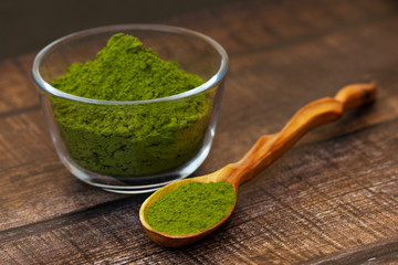 Green tea matcha in a glass bowl and a spoon on a brown wooden background close-up. Matcha in a wooden spoon.