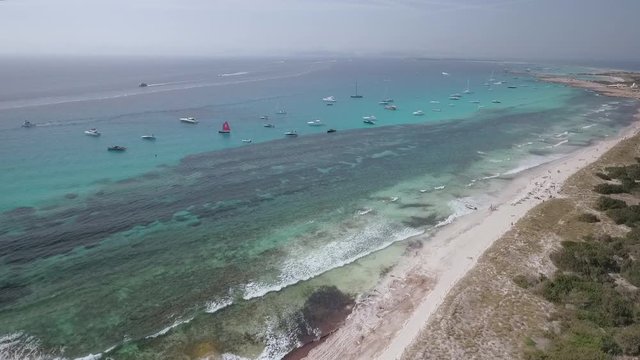 AERIAL DRONE BACKWARD SHOT OF STUNNING PARADISE BEACH AND TURQUOISE CORAL REEF COAST WITH SAILBOATS AND YATHS ANCHORED