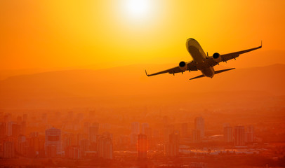 Airplane flying above city at sunset