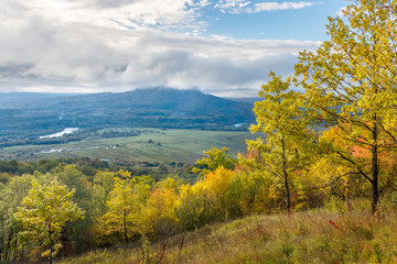 Obraz premium A slope with autumn trees and a valley with a village and agricultural fields at the distance