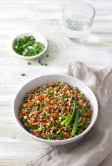 Delicious vegan buckwheat with vegetables and green onions on a light wooden background. Healthy homemade food