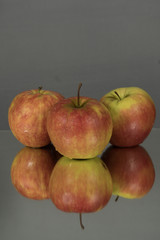 Three red apples on mirroring table on mirror gray background with reflection isolated close up