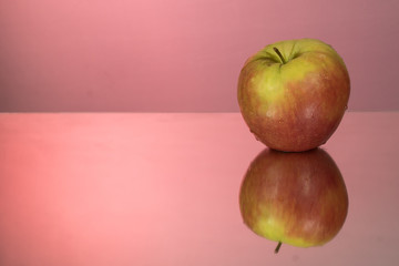 red apple on mirroring table on mirror red background with reflection isolated close up