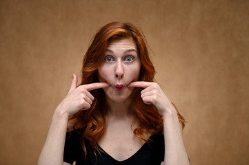Fototapeta premium Studio large photo portrait of Caucasian young actress woman with long red hair on a beige background. Model poses with a smile and grimace.