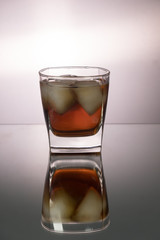 Glass of whiskey with pieces of ice on mirroring table. Vertical image with copy space.