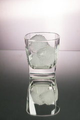 Glass of whiskey with ice cubes in mirror image. Vertical image with copy space.