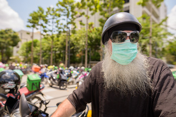 Mature bearded hipster man with sunglasses and mask thinking while riding motorcycle
