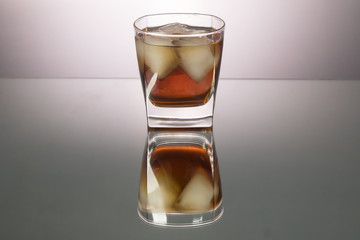Glass of whiskey with pieces of ice on mirroring table. Horizontal image with copy space.