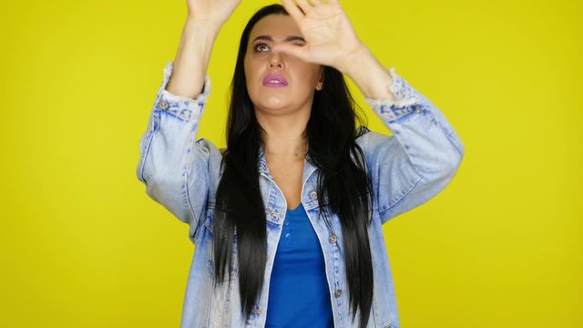 Woman with black hair in a denim jacket shows a pantomime of imaginary glass on a yellow background with copy space. Place for text or product. 4K footage