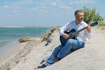 European musician man playing the guitar on the beach in summer