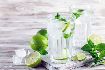Summer cold drink and cocktail. Fresh Mojito cocktail with lime, ice and mint in a glass on white wooden background