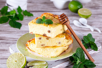 Cottage cheese casserole with raisins, honey and mint, lime slices on a plate on a white table