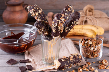 Frozen Chocolate Covered Bananas on a Stick in a glass beaker on wooden table