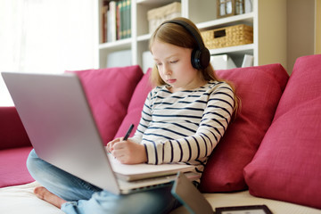 Young schoolgirl doing her homework with digital tablet at home. Child using gadgets to study. Education and distance learning for kids. Homeschooling during quarantine.
