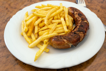 Grilled sausage, German Bratwurst, and french fries on a plate in a fast food restaurant, tasty but unhealthy eating with trans fat and saturated fatty acids, selected focus