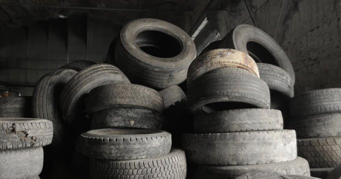Many old rubber car tires in shop of processing recycling plant. Landfill of used automobile wheel tyres. Seasonal car tire replacement. Environmental protection, recycling of used materials.