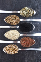 Various Seeds Assortment on dark background. Set of seed: sesame, sunflower, pumpkin, flax, hemp, black cumin in spoons.