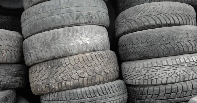 Stacks of many old rubber car tires in shop of processing recycling plant. Landfill of used automobile wheel tyres. Car tire replacement, recycling of used materials. Camera moving from left to right.