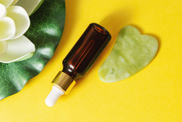 Glass bottle with pipette and jade gua sha at yellow background