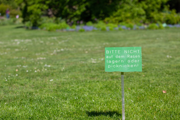 Green sign in German with the text: Please do not lay on the grass or picnic. Background meadow in the park.