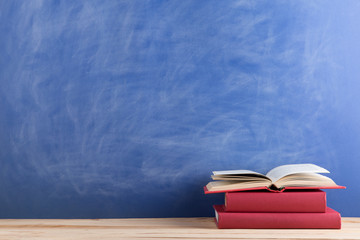Education and reading concept - group of books on the wooden table, blue blackboard background. Teachers desk