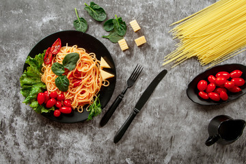 Spaghetti with tomato sauce, cherry tomatoes and basil on a dark background. Tasty appetizing classic italian spaghetti pasta with tomato sauce, cheese parmesan and basil on plate on dark table. 