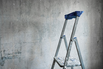 A step ladder smeared with white paint against a gray concrete wall for room repairs.