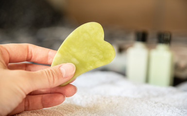 Female hand holding green jade gua sha tool for self massage at home