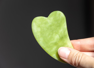 Gua sha tool in natural gemstone of green Jade in hand. Self massage tool