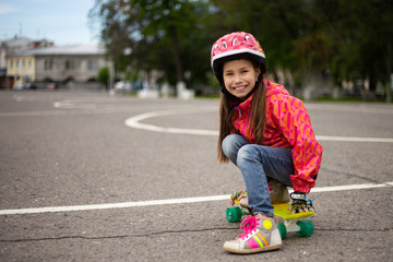 Cute little preteen girl wearing helmet riding on a skateboard in beautiful summer park