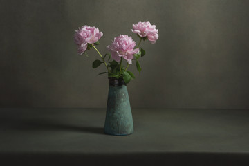 Pink peonies in a vintage pottery vase on a table in a grey room.