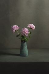 Pink peonies in a vintage pottery vase on a table in a grey room.