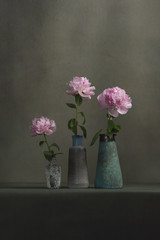 Three vintage pottery vases with pink peonies on a table in a grey room.