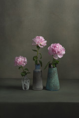 Three vintage pottery vases with pink peonies on a table in a grey room.