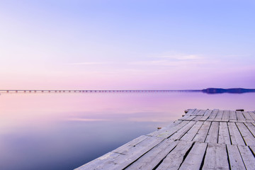 Pier on the background of the sea with a glossy surface, which reflects the pink-blue sky