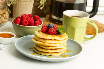 Tortitas apiladas en un plato redondo gris con frutos rojos, arándanos y frembuesas  con taza de café sobre una mesa en la cocina. Vista superior y de cerca
