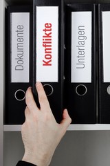 Konflikte – Finanzen/Statistik. Ordner im Büro-Regal. Hand greift Unterlagen im Schrank. Beschriftung mit Wort