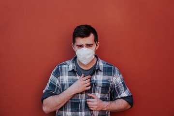 a guy in a checked shirt and mask on a red background looks at the camera.
