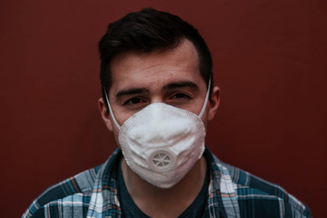 a masked man looks at the camera on a dark red background