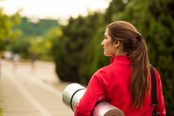 a young Caucasian woman goes to training with a yoga Mat. Against the background of the Park. Rear view