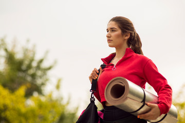 a young Caucasian woman goes to training with a yoga Mat. Against the background of the Park. Gray sky