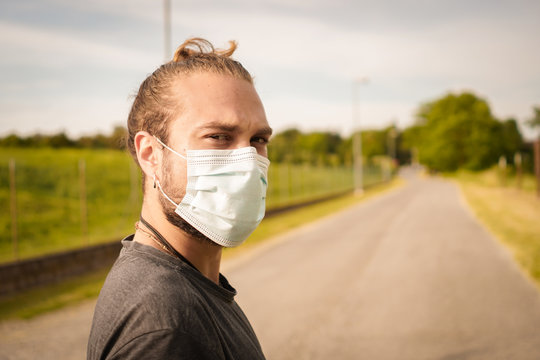 Blond Boy With Long Hair Rests After Doing Physical Activity During The Quarantine. Wear The Coronavirus Protective Mask