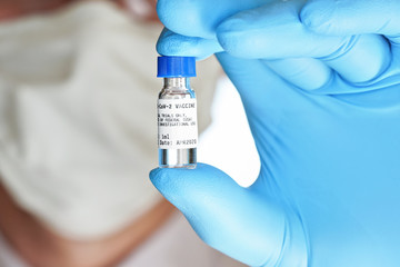 Hand in blue medical gloves holding small vial with label that says Cov-2 vaccine (sticker is own...