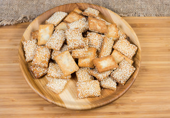 Flat flaky sesame cookies on wooden dish on wooden surface