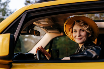 Beautiful Young Woman Driving Yellow Taxi Car. Happy Blonde Female Smile in Hat Looking at Camera....