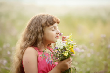 Fototapeta premium a pretty girl in a pink blouse sniffs a bouquet of flowers in the field. sunset in the background. portrait. close up.