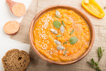 Sweet potato or batata cream soup with sesame seeds in a wooden bowl on a white wooden background. top view, selective focus.