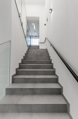 Fototapeta na wymiar Clean white stairway staircase with glass railing in corridor in office building 